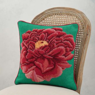 A needlepoint cushion of a bright red peony set on a green background photographed on a chair