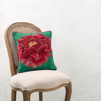 A needlepoint cushion of a bright red peony set on a green background photographed on a chair